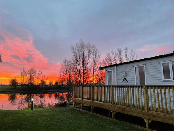 One of the static caravans for sale in North Yorkshire at Brickyard Lakes overlooking the lake and a sunset sky